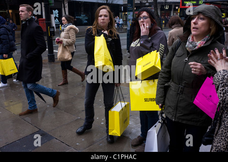 Shopping femmes portent leurs achats dans des sacs jaunes Selfridges Oxford Street à Londres. Banque D'Images