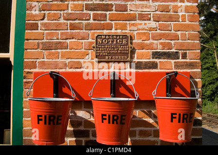 L'Angleterre, Norfolk, Weybourne, trois seaux d'incendie rouge sur le mur Banque D'Images