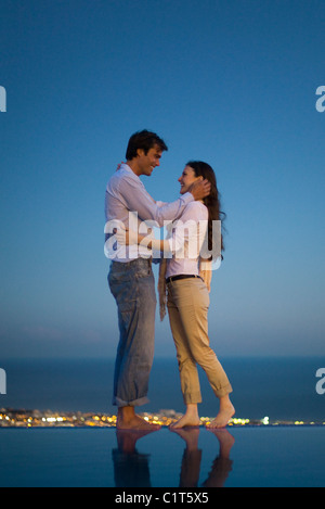 Couple au bord de la piscine à débordement au crépuscule Banque D'Images