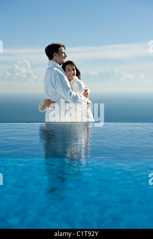 Couple à bord d'une piscine à débordement, les deux portant des peignoirs Banque D'Images