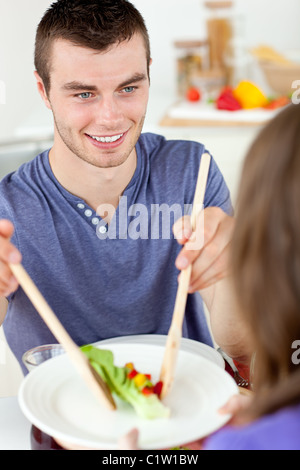 Homme heureux de mettre sur une assiette de salade à table avec sa petite amie dans la cuisine Banque D'Images