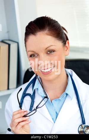 Happy female doctor holding glasses smiling at the camera Banque D'Images