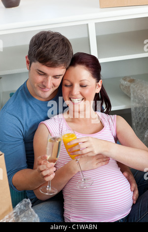 Joyful couple expecting a baby boire et assis sur le plancher Banque D'Images