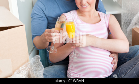 Smiling couple expecting a baby boire et assis sur le plancher Banque D'Images