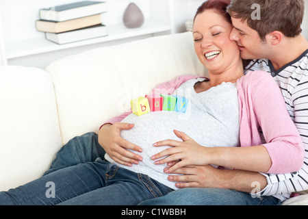 Portrait d'une femme enceinte avec merry bébé cubes sur son ventre et de son mari l'embrasser Banque D'Images