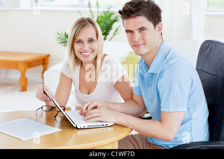 Superbe couple travaillant ensemble sur l'ordinateur portable assis à une table dans leur salon Banque D'Images