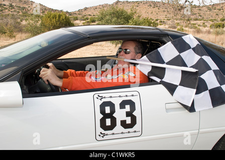 Pilote de voiture de course de Mike pouvoirs, ceux de l'équipe de course automobile, garantit une victoire en menant son propre drapeau à damiers ! Alpine, Texas. Banque D'Images