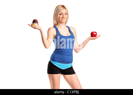 Une femme tenant une pomme et tranche de gâteau en essayant de décider lequel de manger Banque D'Images