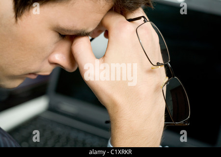 Photo de l'homme de la fatigue avec ses lunettes au large de garder sa main près de visage après une dure journée de travail Banque D'Images