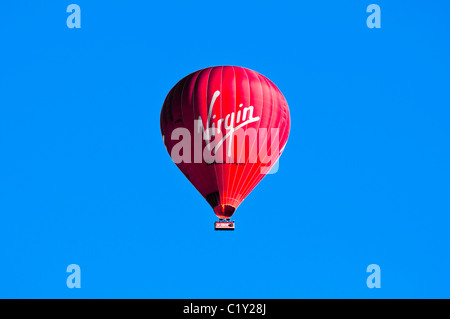 Red Hot Air Balloon contre ciel bleu profond avec logo vierge clairement visible. UK. Banque D'Images