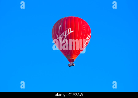 Red Hot Air Balloon contre ciel bleu profond avec logo vierge clairement visible. UK. Banque D'Images