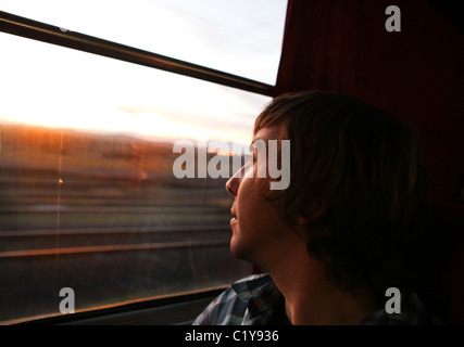 Jeune homme regardant par la fenêtre sur un voyage en train tôt le matin Banque D'Images