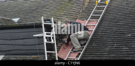 WORKMAN TRAVAILLE SUR DES ÉCHELLES SUR LA CHAMBRE A LA RÉFECTION DU TOIT PASSAGE AU NUMÉRIQUE ANALOGIQUE SIGNAL ANTENNES NOUVEAU COUPER ETC UK Banque D'Images