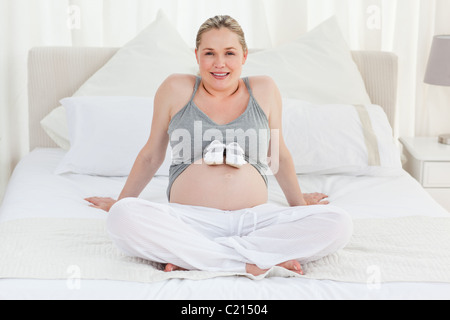 Femme enceinte joyeuse avec des chaussures pour enfants sur son ventre Banque D'Images