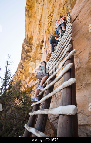 Une femme pose pour une photo sur une échelle menant au balcon Chambre cliff demeure dans le Parc National de Mesa Verde, Colorado, USA. Banque D'Images