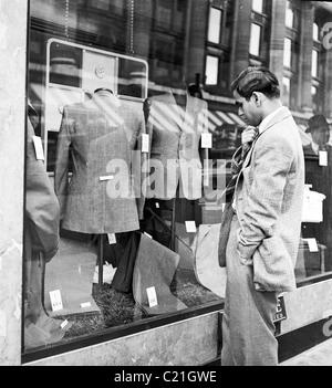 1950, un homme nouvellement arrivé immigré au Royaume-Uni regardant une vitrine dans une boutique de vêtements à Londres dans cette photo historique de J Allan Cash. Banque D'Images