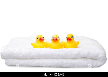 Trois canards en caoutchouc jaune dans une rangée sur une serviette blanche pelucheuse isolé sur fond blanc Banque D'Images