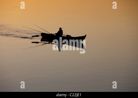 Pêche en bateau à rames / skiff / canot au coucher du soleil sur la rivière Oulujoki Finlande Banque D'Images