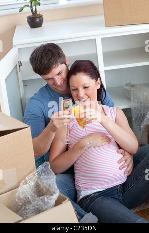 Cheerful couple célébrant la grossesse et dépose avec champagne assis sur le plancher Banque D'Images