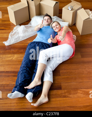 Heureux couple gisant par terre dans leur nouvelle maison doing thumbs-up Banque D'Images