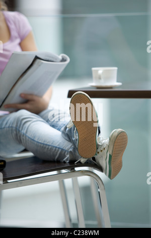 Jeune femme assise avec les pieds jusqu'reading magazine Banque D'Images