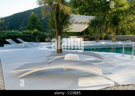 Transats modernes sur terrasse en pierre d'une piscine extérieure Banque D'Images