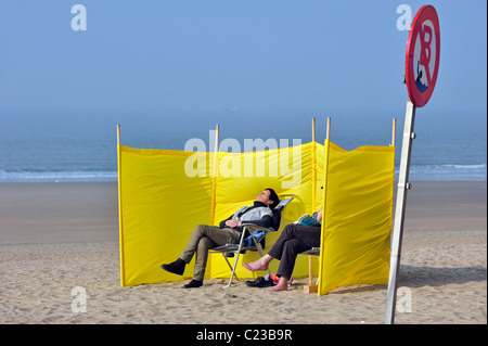 Les touristes de soleil derrière le brise-vent sur la plage, au début du printemps, Ostende, Belgique Banque D'Images