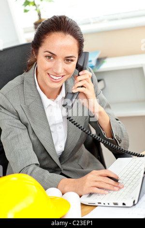 Confident female architect parlant au téléphone et en utilisant son ordinateur portable dans son bureau Banque D'Images