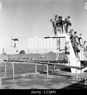 Angleterre, années 1950. Photographie par J Allan Paiement d'un groupe de garçons sur la plate-forme à une piscine extérieure. Banque D'Images