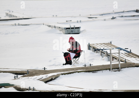 Un pêcheur sur glace solitaire travaille avec sa ligne tout en restant assis sur la surface gelée du Montrose Harbor Chicago, Illinois, USA. Banque D'Images