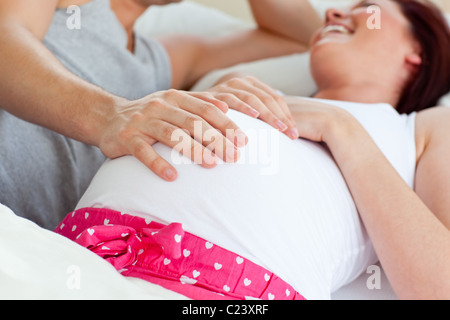 Cheerful pregnant woman lying on bed with son mari Banque D'Images