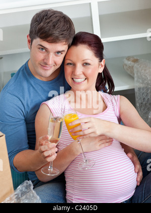 Heureux couple expecting a baby boire et assis sur le plancher Banque D'Images