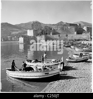 Années 1950, France. Collection de petits bateaux de pêche amarrés sur Beach à côté du vieux fort de Collioures dans ce tableau historique. Banque D'Images