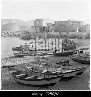 Années 1950, France. Les bateaux de pêche amarrés sur la plage à Collioures, France avec la vieille forteresse à distance dans ce tableau historique. Banque D'Images