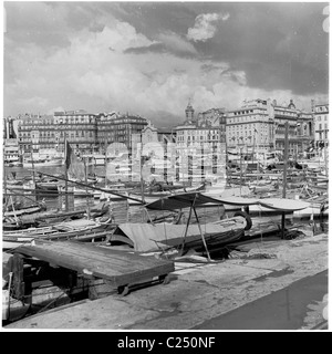 1950s, petits bateaux de pêche amarrés dans le port du vieux port de Marseille, France, avec les bâtiments de la ville ancienne en arrière-plan. Banque D'Images