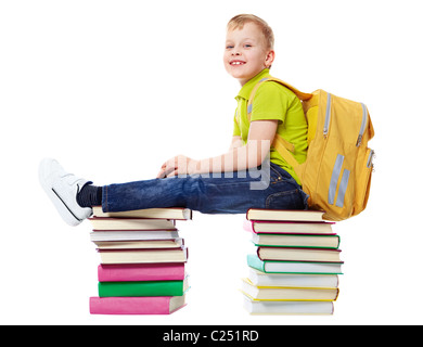 A smiling boy with satchel assis sur deux tas de livres Banque D'Images