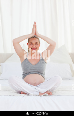 Pregnant woman practicing yoga on her bed Banque D'Images