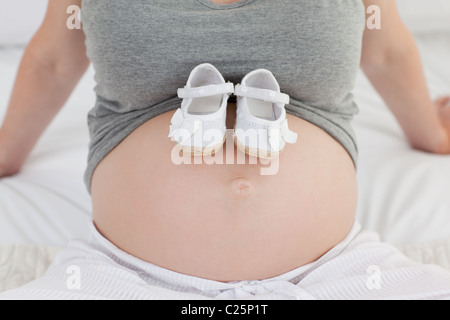 Femme enceinte joyeuse avec les chaussures pour enfants sur son ventre Banque D'Images