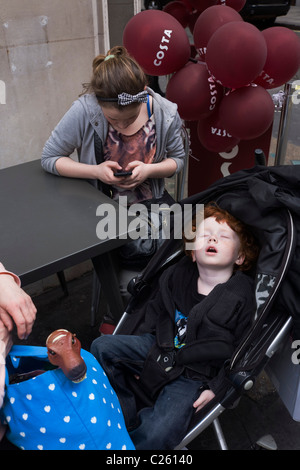 Un garçon aux cheveux auburn à dormir à poings fermés dans son buggy dort pendant une excursion à Londres. Banque D'Images