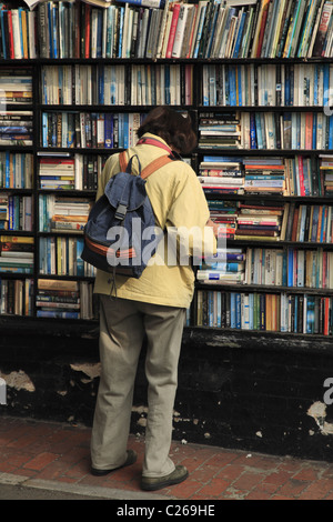 Une femme lisant attentivement les rayons de livres à l'extérieur d'une librairie de seconde main à Eastbourne, East Sussex, Angleterre. Banque D'Images