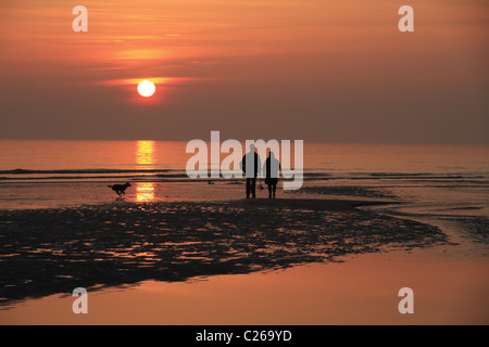 Un couple voir le coucher du soleil sur la mer à Urrugne, East Sussex, Angleterre. Banque D'Images