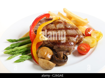 Steak de surlonge de veau, servi avec des asperges, tomates cerises, champignons grillés, des rubans rouges et jaunes de capsicum et de frites. Banque D'Images