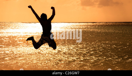 Heureux Jeune homme sautant sur la plage au coucher du soleil Banque D'Images