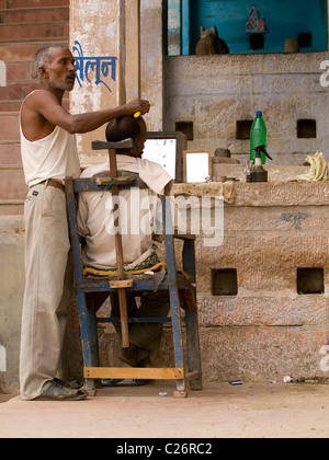 Coiffure couper les cheveux d'un homme sur l'un des du ghat de Varanasi, Inde Banque D'Images