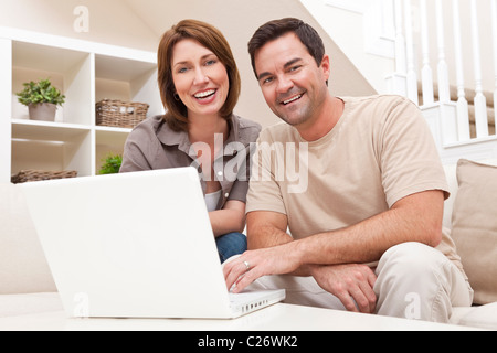 Happy man and woman couple dans la trentaine, assis ensemble à la maison sur un canapé à l'aide d'un ordinateur portable Banque D'Images