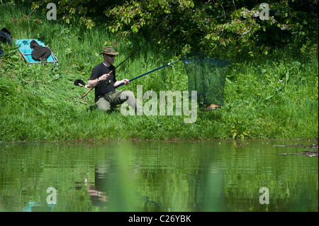 Un jeune pêcheur attraper une carpe dans son filet de l'atterrissage. Angleterre, Royaume-Uni Banque D'Images