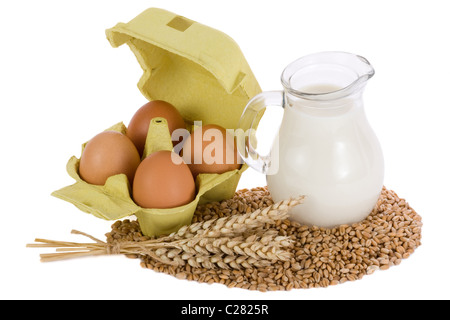 Verseuse en verre avec du lait, les épis de blé et d'oeufs sur fond blanc Banque D'Images