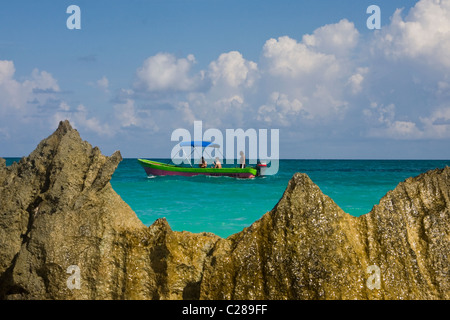 Un bateau coloré de manoeuvres dans la mer des Caraïbes avec les touristes et une formation rocheuse au premier plan, près de la Playa Tulum Mexico Banque D'Images