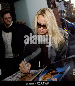 Pamela Anderson enveloppée dans un foulard et de signer des autographes pour les fans en arrivant au Nouveau théâtre de Wimbledon, où elle est Banque D'Images