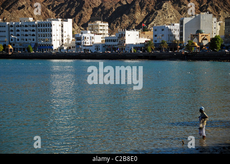 Oman, Muscat, un homme debout omanais locaux dans l'eau et en regardant le magnifique panorama de la mer et la zone portuaire Muttrah Banque D'Images